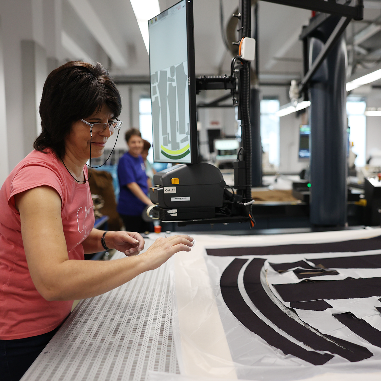 Person working with fabric and a large screen printer in a factory setting